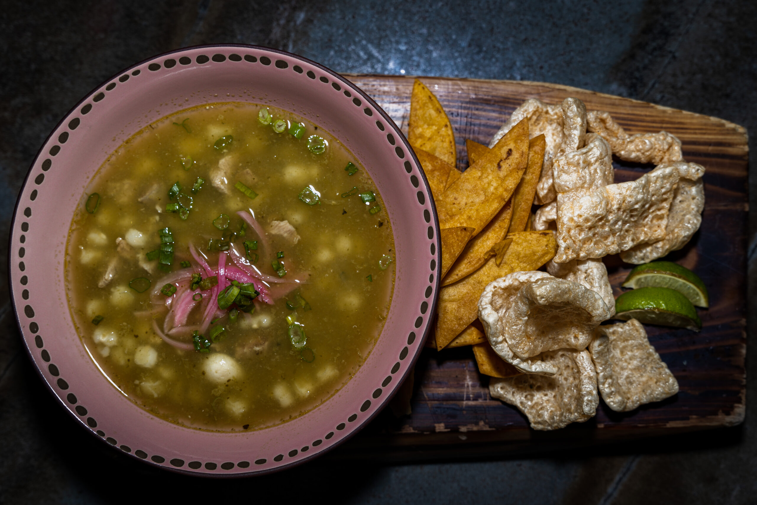 A vibrant bowl of authentic Pozole Verde in Las Vegas served with hominy, pork, tortilla strips, chicharrones, and lime - perfect for diners searching for the best green pozole nearby.